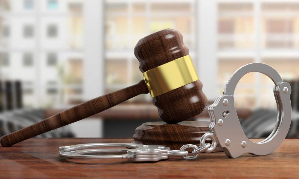 Metal police handcuffs and judge gavel on wooden desk, blur office background. 3d illustration